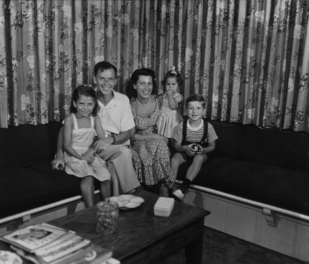 Frank Sinatra sitting on a couch with his first wife, Nancy Barbato, and their children Nancy, Tina, and Frank Jr. 
