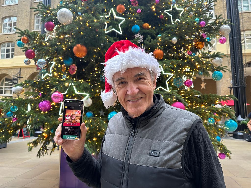 Larry Lamb in a Santa hat holding a mobile phone