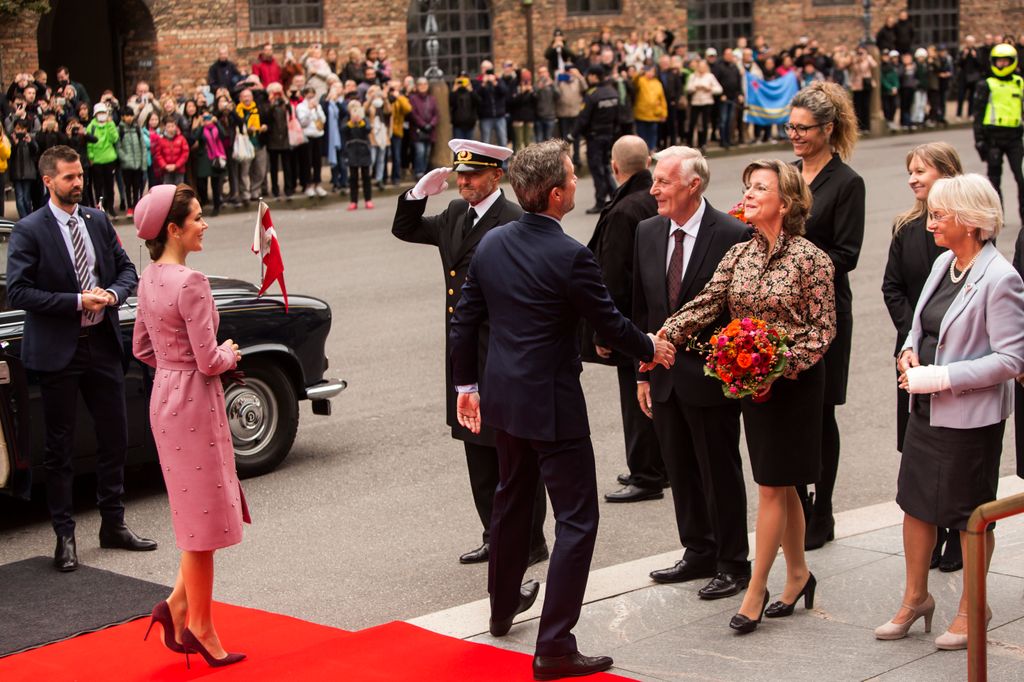 Queen Mary in pink greeting people outside parliament