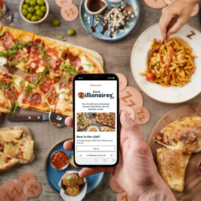 someone holds the zillionaires app open on their phone over a table filled with Italian food