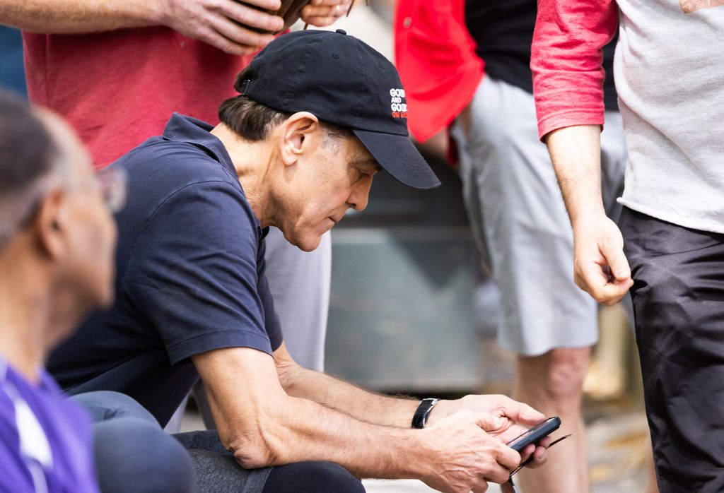 George Clooney sitting down and looking at his phone while takign break from playing softball in NYC