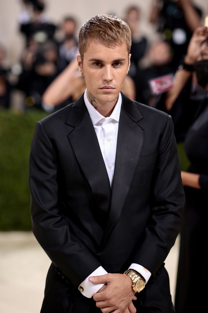 Justin Bieber with his hands crossed standing in a suit while walking red carpet at the MET Gala