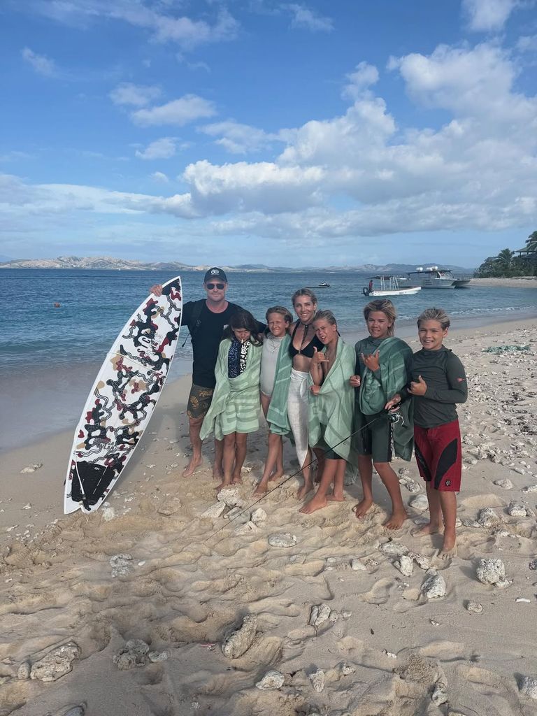 Chris Hemsworth and Elsa Pataky posing on beack with their sons and surfboard