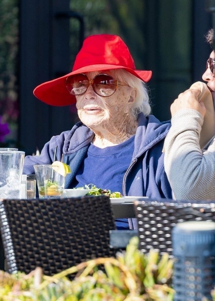 Shirley wearing red hat and dining outside with a cocktail
