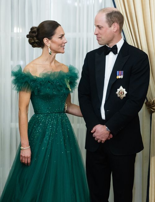 kate turns towards william who is dressed in black tie while she wears a sparkly green ballgown with an pff the shoulder frill and her large diamond earrings have prominent emeralds which match the dress