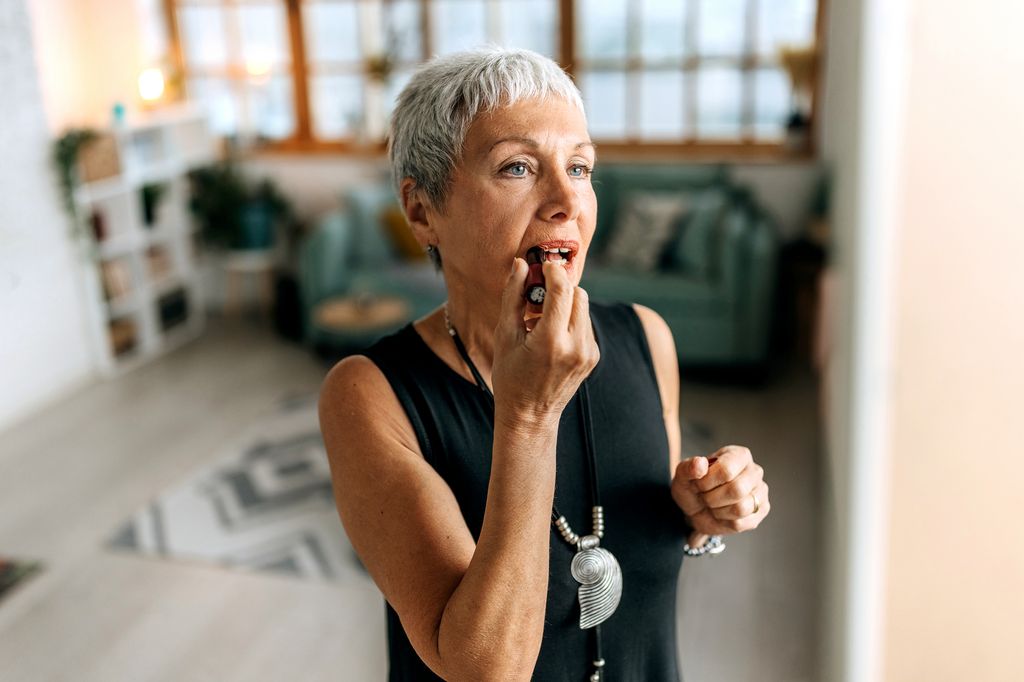 Well dressed senior woman applying lipstick at home. getting ready for night out