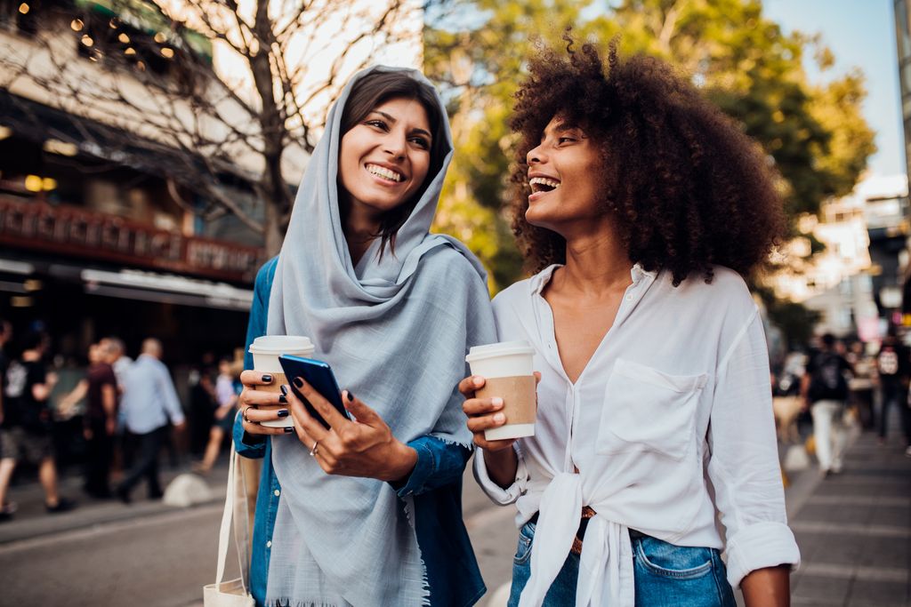 Portrait of two beautiful girls drinking coffee and surfing the net at the street.