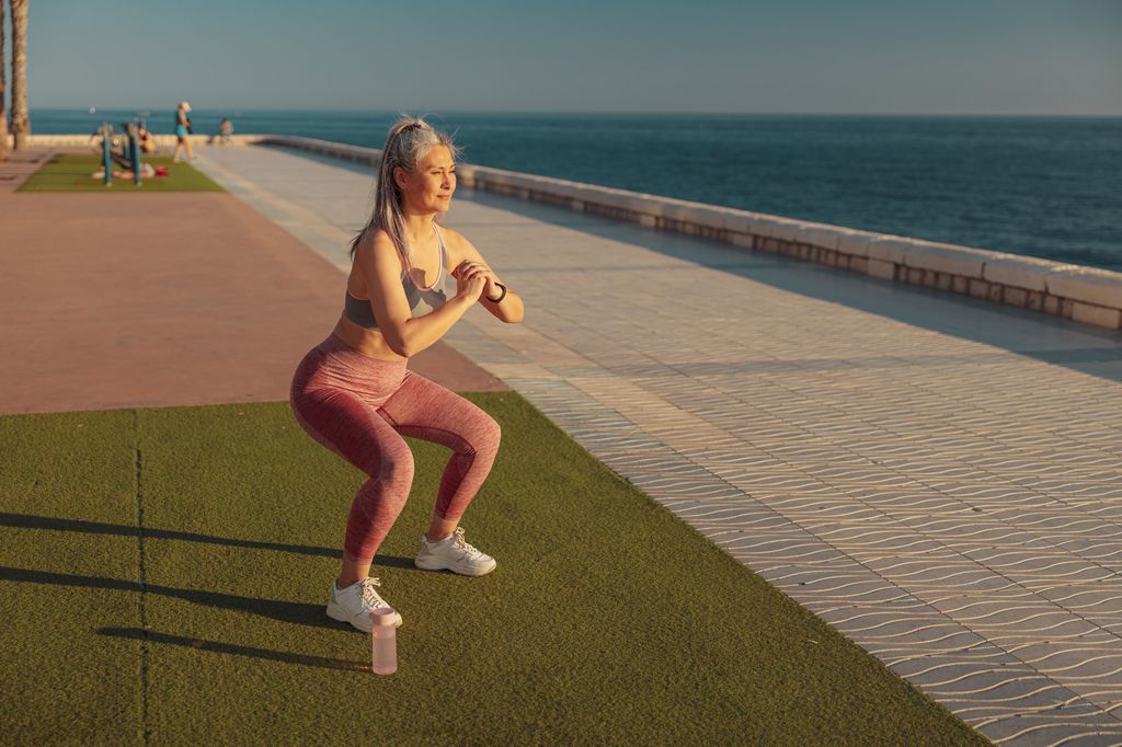older woman doing squats at the beach