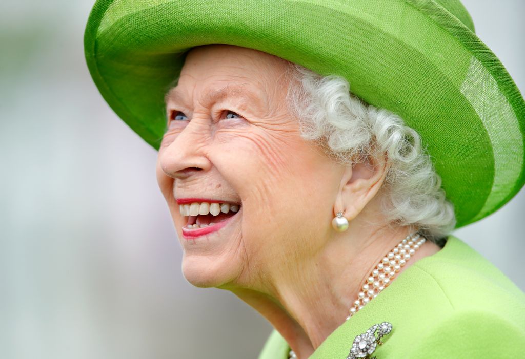 queen smiling in green coat and hat 