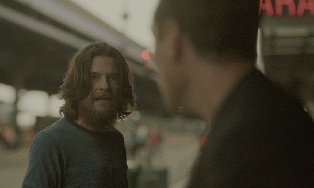 man with long hair looking at another man