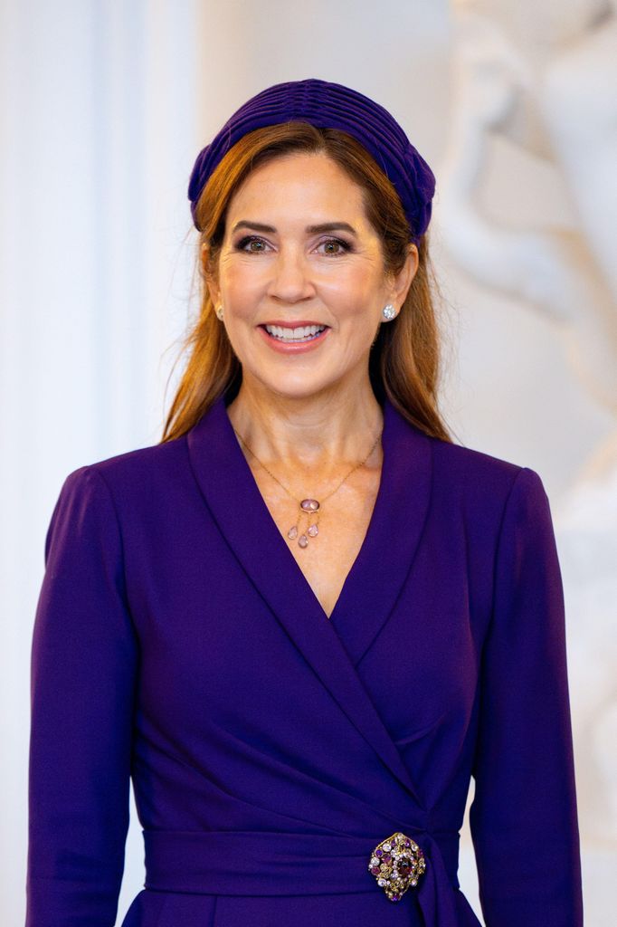 Queen Mary sorrindo com vestido roxo e bandana