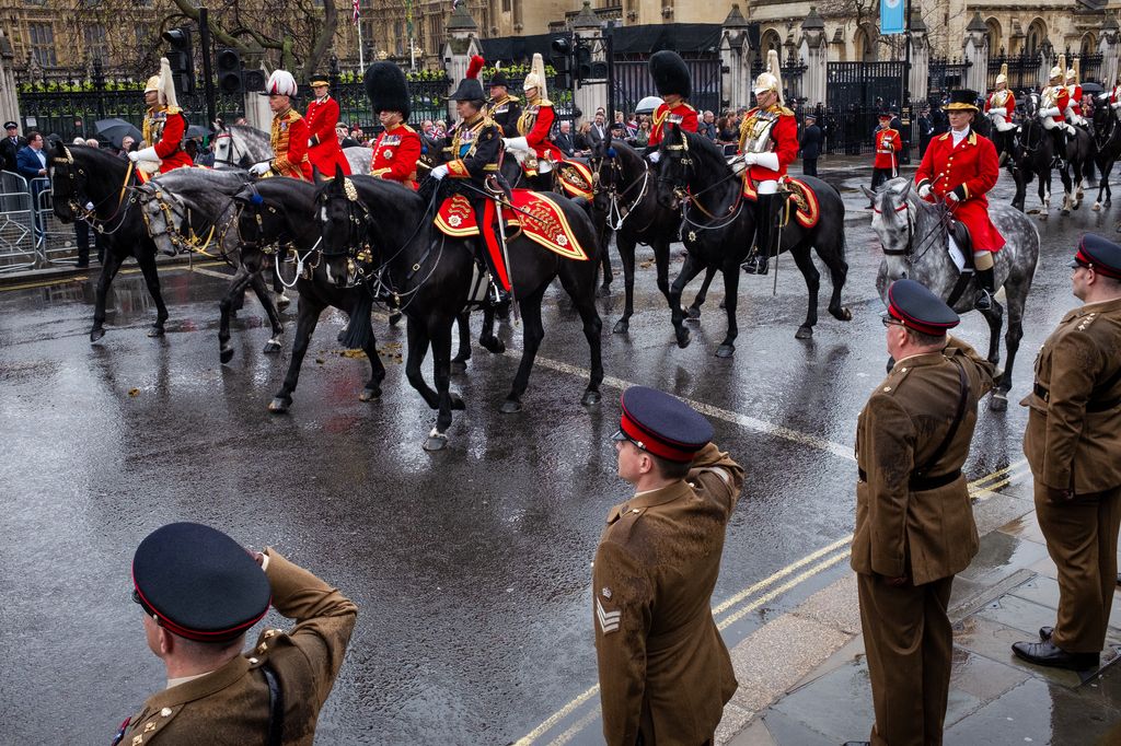 Black horses being ridden past saluting military personnel