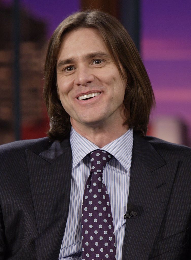 Jim Carey sourit lors d'un chatshow dans une chemise rayée et une cravate à pois.