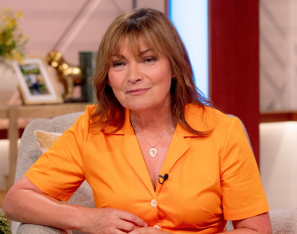 Lorraine Kelly sits on sofa wearing orange shirt
