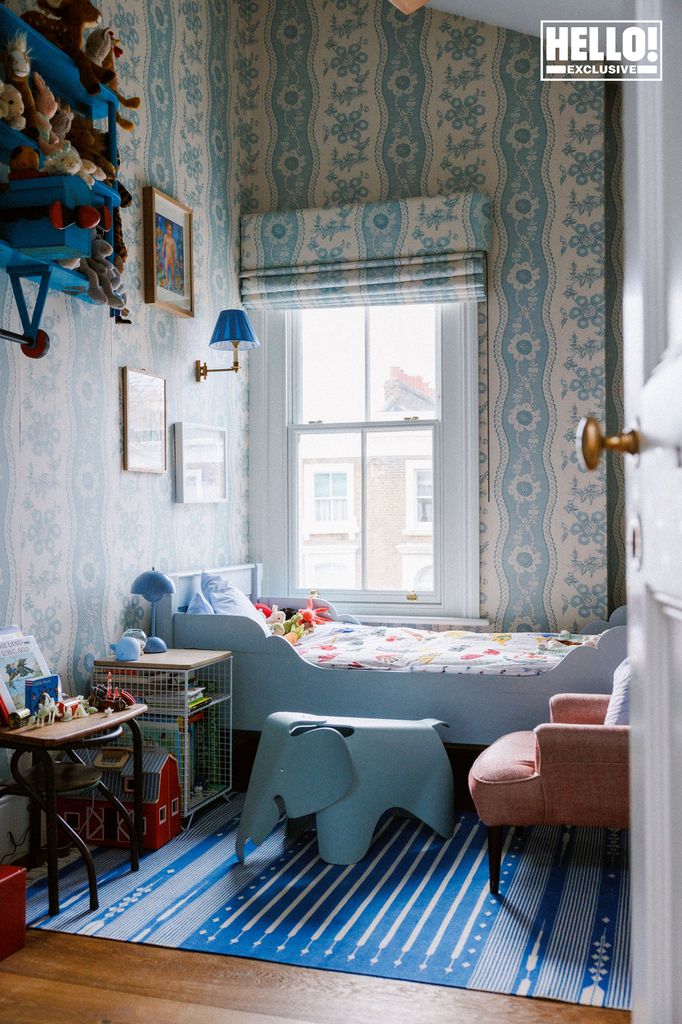 Nina Litchfield's son's bedroom at Notting Hill home. A cheerful child's bedroom with blue patterned wallpaper, a blue bed, and a blue striped rug. There is a pink armchair and an elephant-shaped toy in the room.