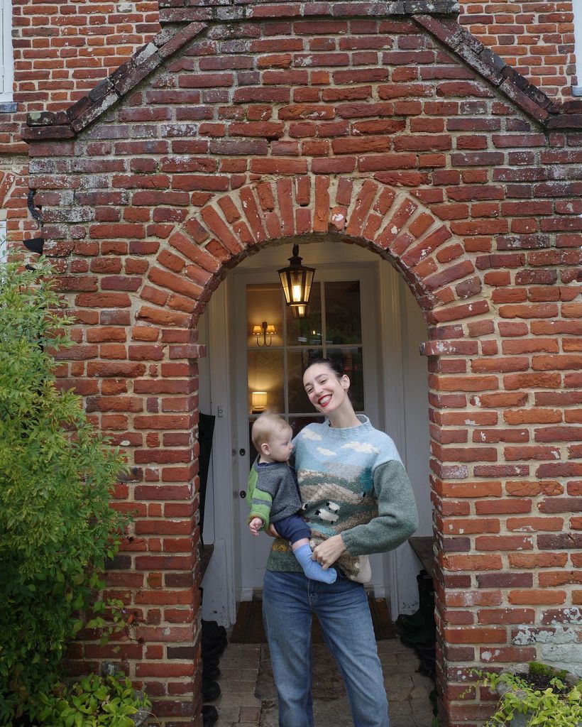 Laura outside brick house holding baby