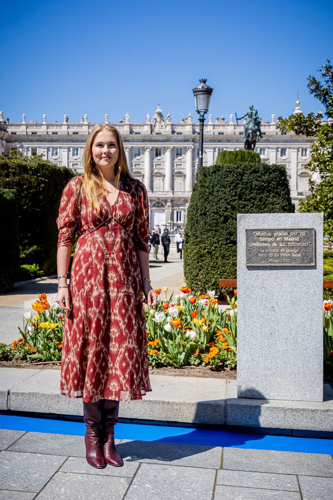 princess amalia in red dress and leather boots standing next to plaque