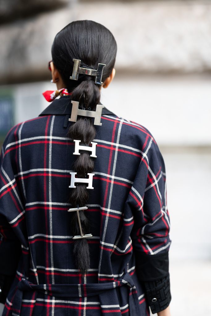 : A guest wears Hermes silver hair accessories and a blue, red and white checked coat outside Hermes show during Womenswear Spring/Summer 2025 as part of  Paris Fashion Week 