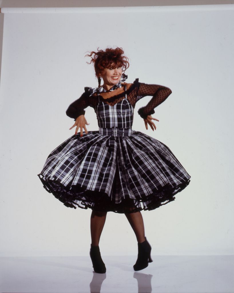 Portrait of American fashion designer Betsey Johnson, posed against a white background anf dressed in black and white tartan and lace, as she makes a face, late 1980s or early , 1990s