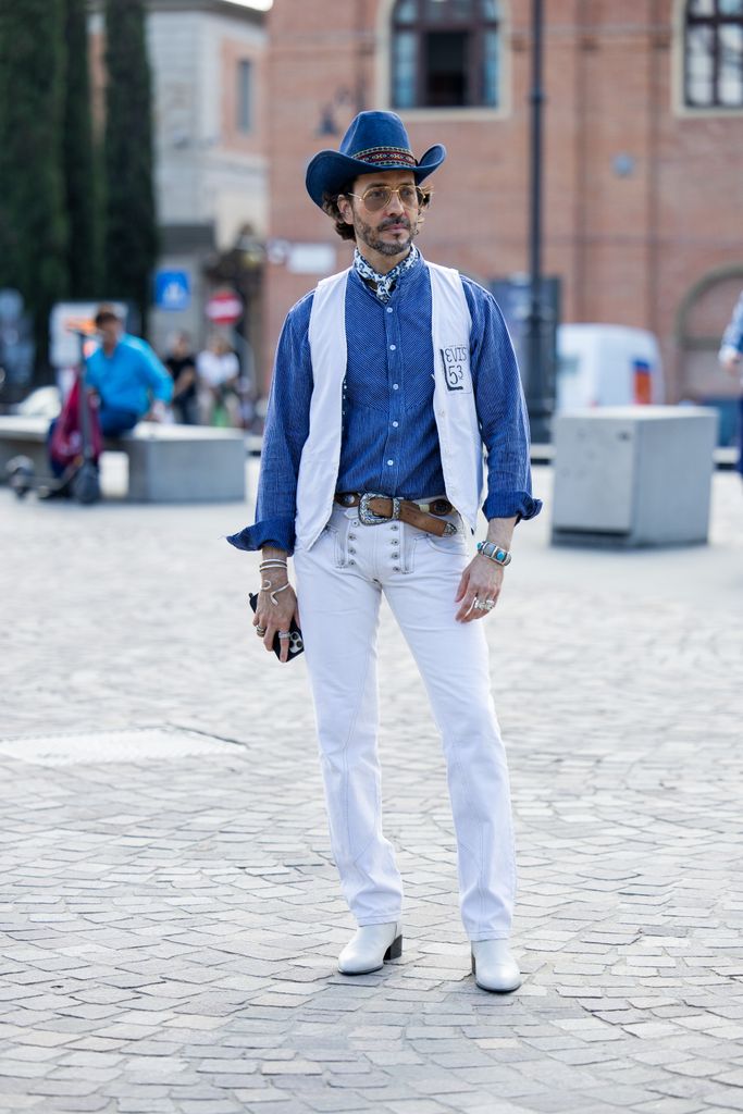 Un invité porte un chapeau de cowboy bleu, un gilet, une chemise en jean et un pantalon blanc lors du Pitti Immagine Uomo 106