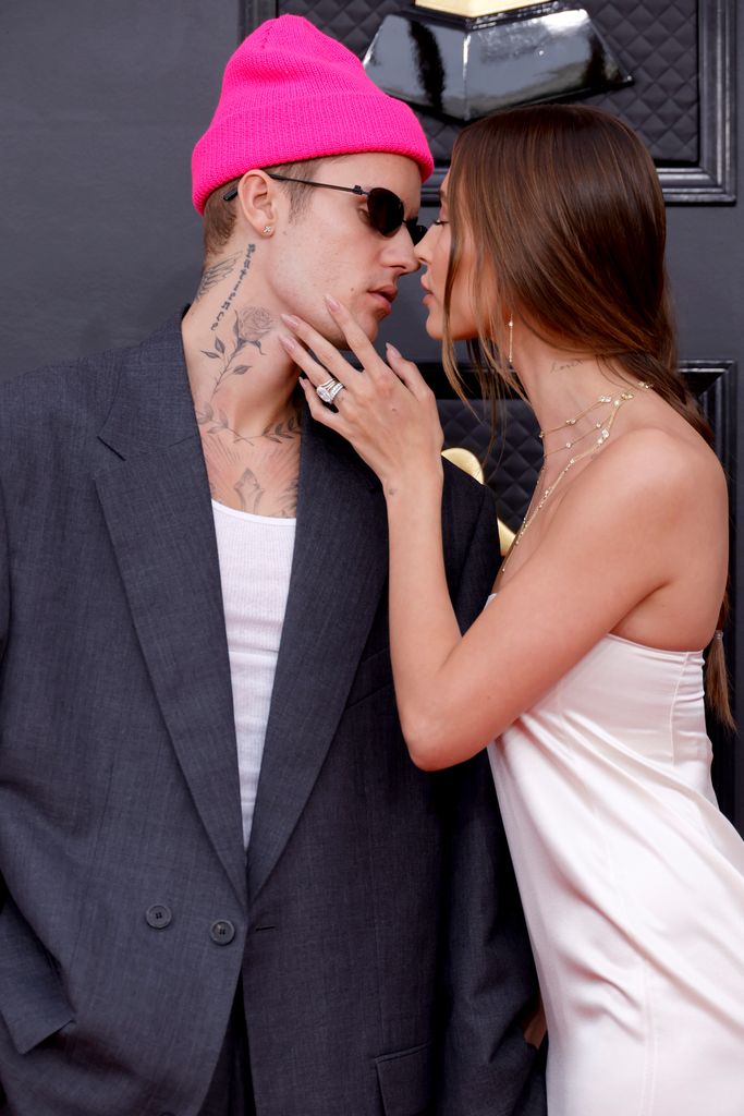 Hailey Bieber in a white dress kissing her husband Justin in a pink hat