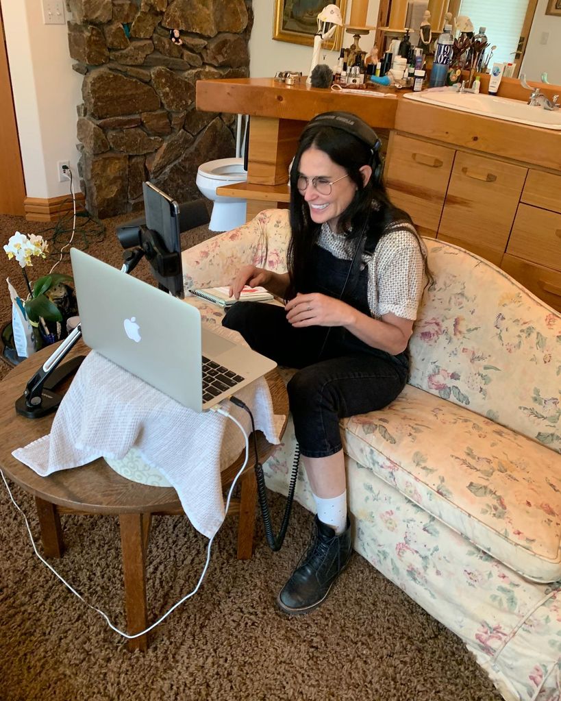 Demi Moore on laptop in room with bare brick walls