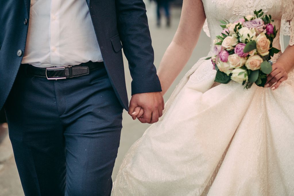  Wedding bouquet in hands of bride and groom. Wedding couple is walking holding hands. In white dress and blue jacket.