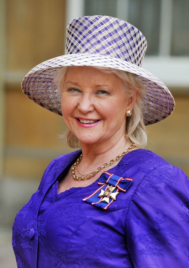 Angela Kelly wearing a big blue hat and blue outfit whilst smiling at the camera