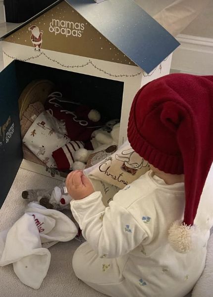 A baby girl wearing a Santa's hat and a cream-coloured onesie