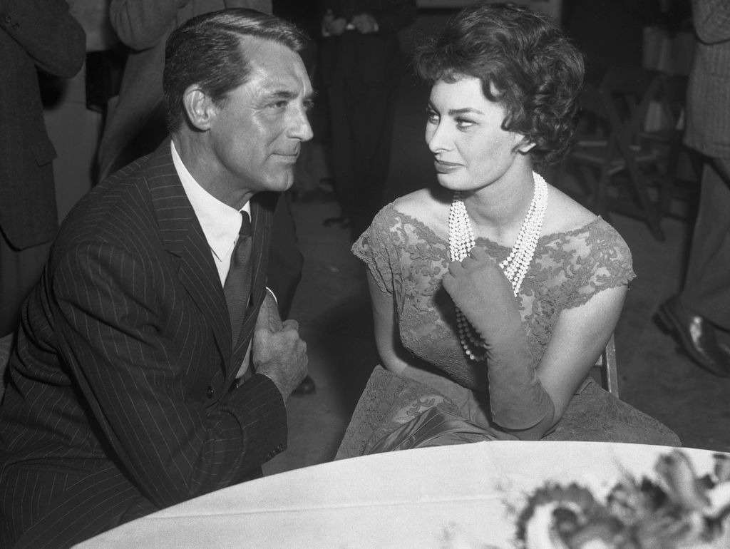Sophia Loren with a pearl necklace sitting at a table with Cary Grant