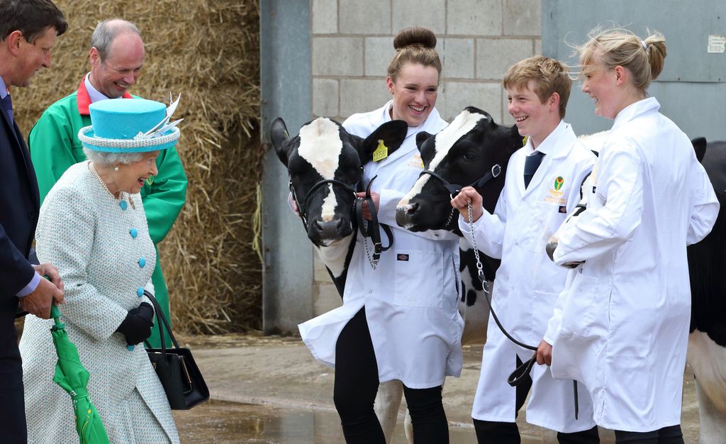 The Queen smiling at sudents and two dairy cows