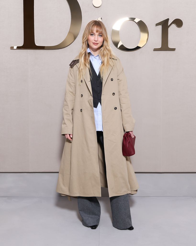 Jennifer Lawrence in trench coat in front of dior sign
