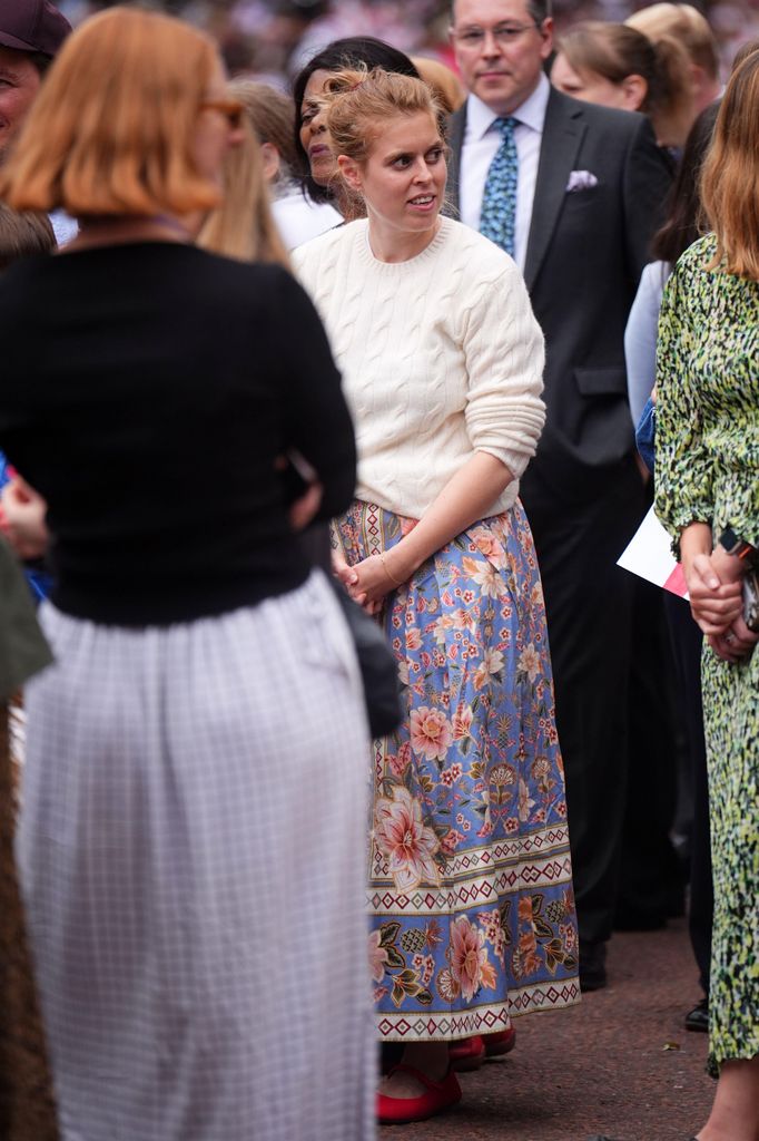 Princess Beatrice in a crowd in a white jumper and floral skirt