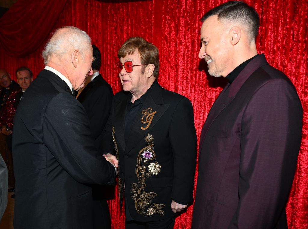 King Charles shaking hands with Elton John as David Furnish looks on