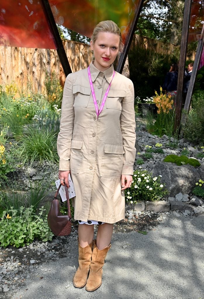 Parker Lapaine in a beige safari-style shirtdress with cowboy boots poses in front of floral installations.