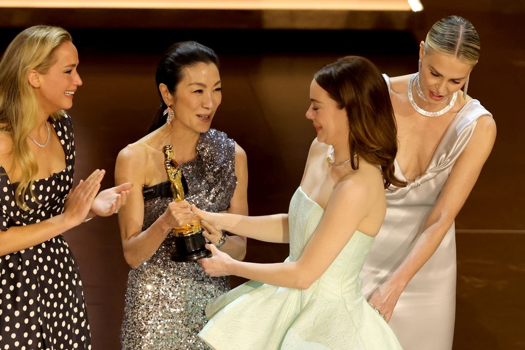 HOLLYWOOD, CALIFORNIA - MARCH 10: Emma Stone (2nd R) accepts the Best Actress in a Leading Role award for "Poor Things" from Jennifer Lawrence, Michelle Yeoh, and Charlize Theron onstage during the 96th Annual Academy Awards at Dolby Theatre on March 10, 2024 in Hollywood, California. (Photo by Kevin Winter/Getty Images)