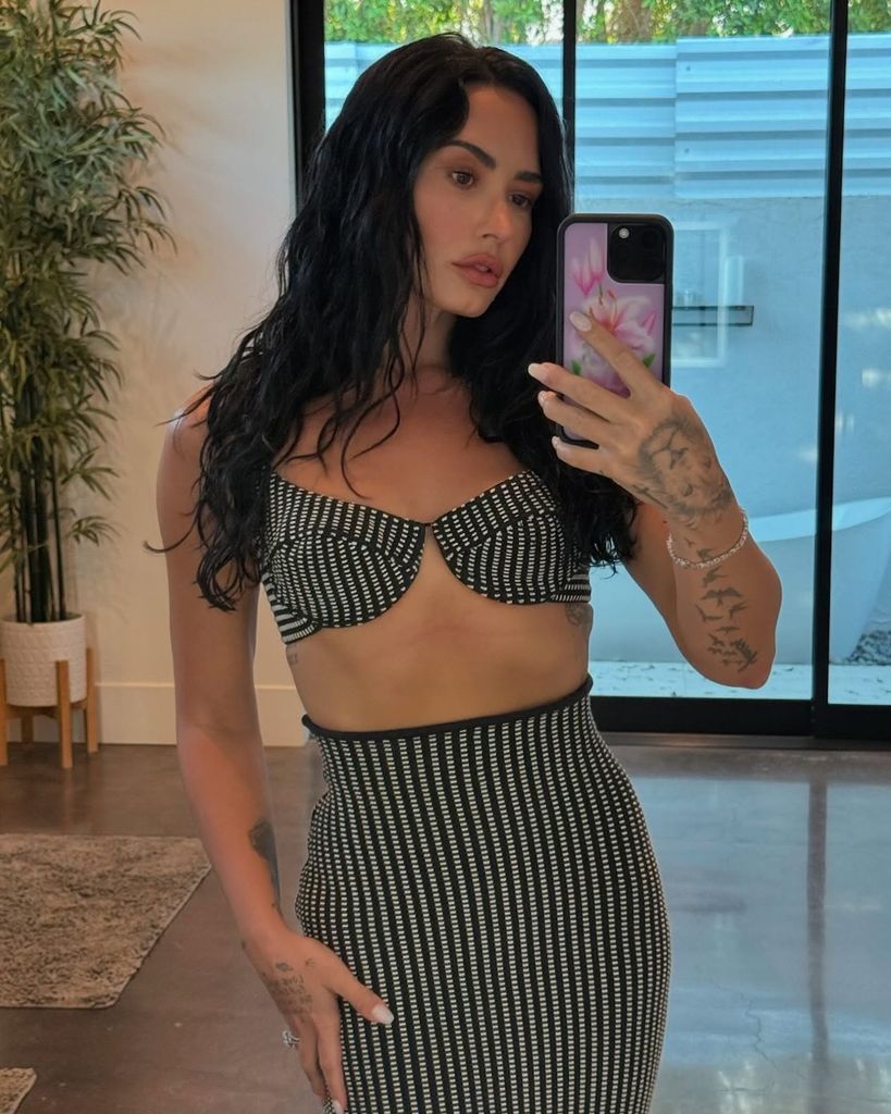 photo of demi lovato posing for selfie wearing monochrome skirt and bra top