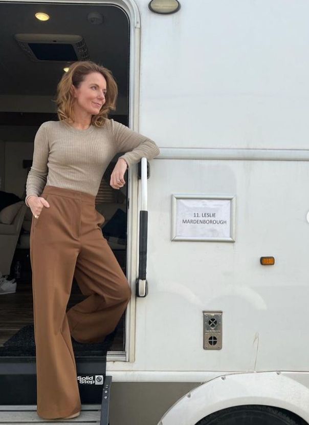 Geri Halliwell-Horner standing outside a film trailer in beige jumper and brown trousers