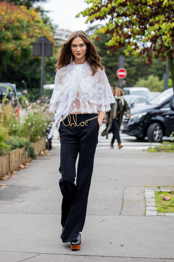  Karlie Kloss wears white laced blouse, golden logo belt, black pants outside Chloe during Womenswear Spring/Summer 2025 as part of  Paris Fashion Week