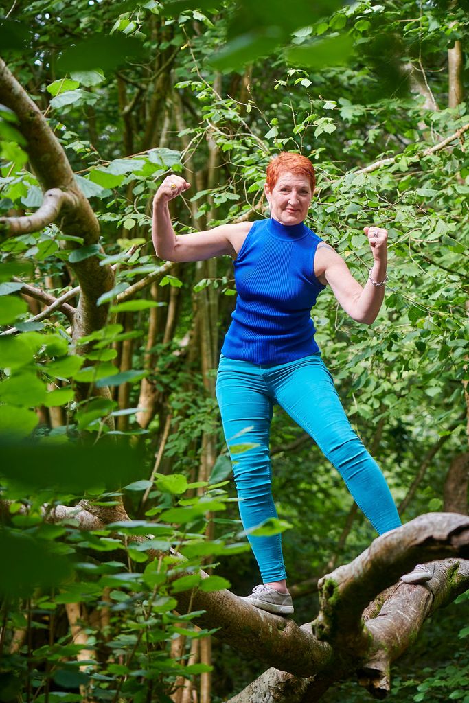 woman in blue top and trousers flexing her muscles in a tree