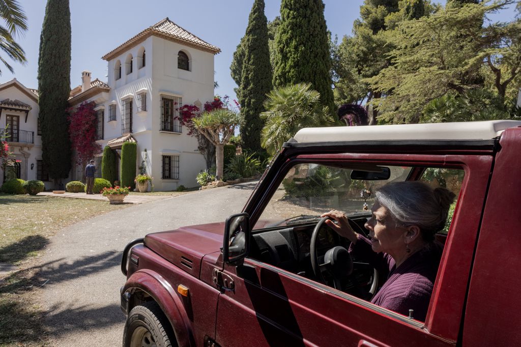 a woman drives a red car up to a white house