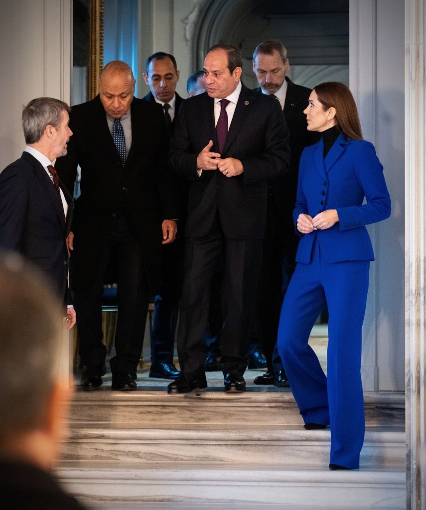 queen mary descending steps in cobalt suit talking to men