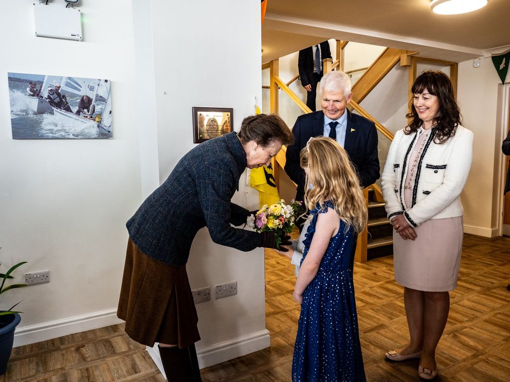 Princess Anne bending down to receive a bunch of flowers 