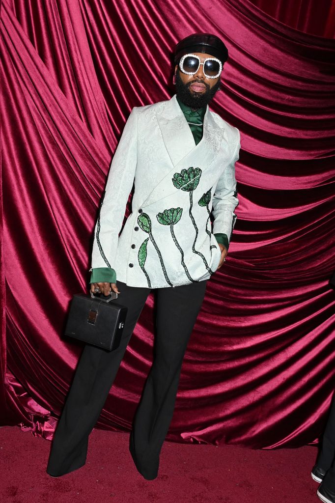 Swanky Jerry in a floral-embroidered white blazer, green shirt, and black flares with oversized pearl sunglasses at 2025 Met Gala after-party.