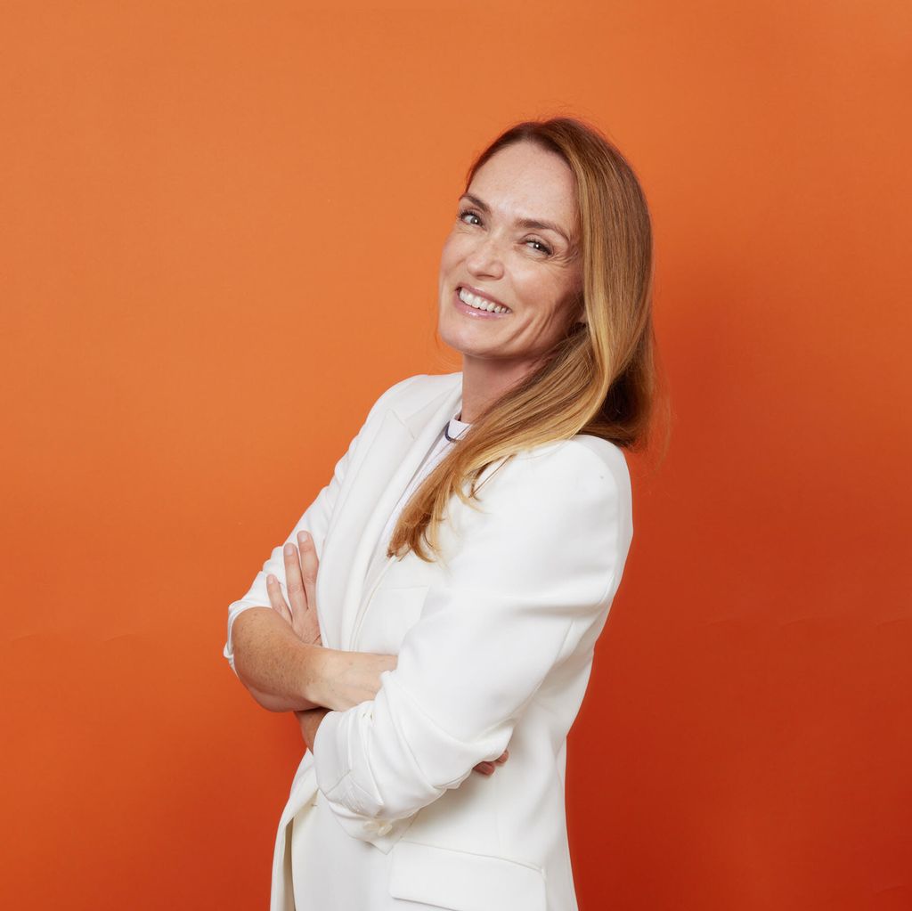 woman smiling in a white jacket in front of an orange background 