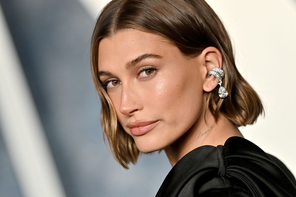 Hailey Bieber looking over her shoulder wearing a black dress at Oscars party