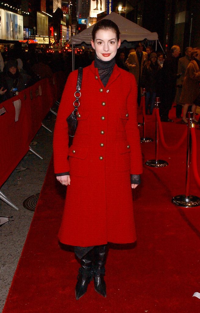 Anne Hathaway on a red carpet wearing a red coat, knee-high boots and red lipstick