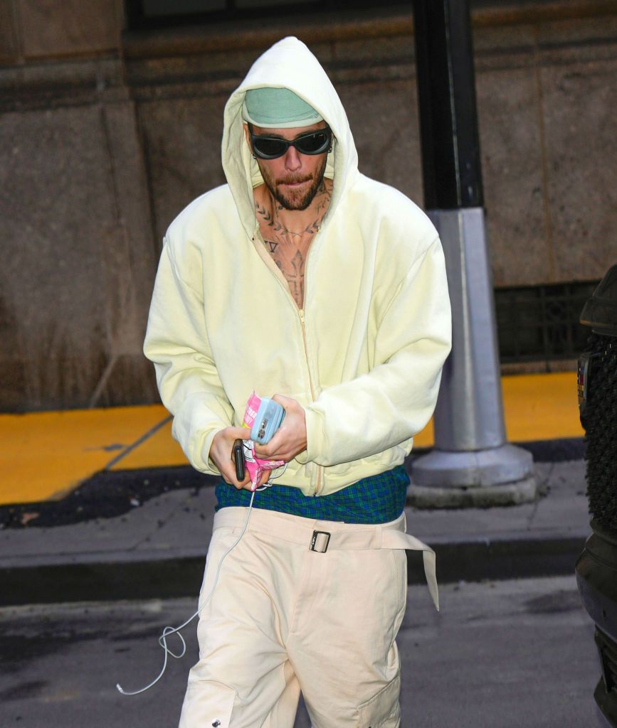 Justin Bieber wearing yellow hoody and baggy trousers walks awar from car in NYC