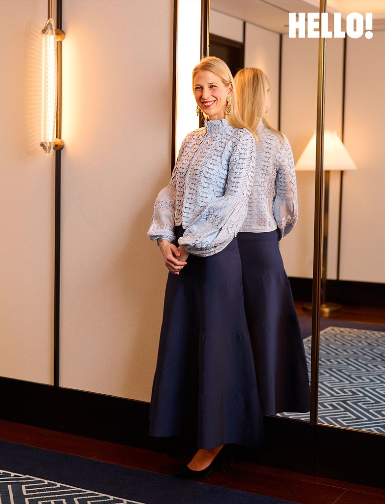 Lady Gabriella Windsor smiles while standing for a photograph in a light blue jacket and dark blue dress
