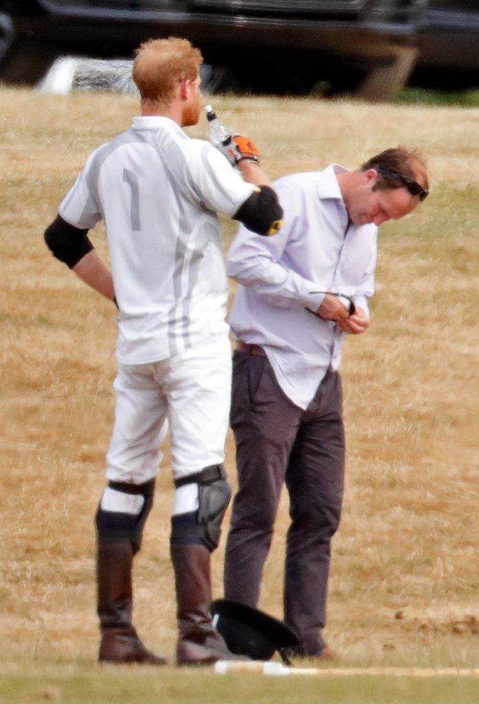 Prince Harry, Duke of Sussex drinks a bottle of water whilst he has his sunglasses cleaned for him by his polo manager Andrew Tucker during the Audi Polo Challenge at Coworth Park Polo Club